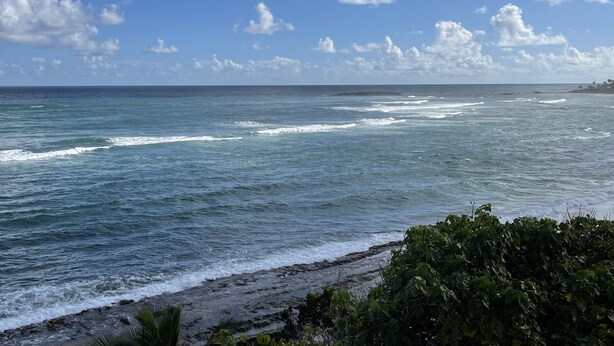 Ein Strand mit Wellen, blauem Himmel und vereinzelten Wolken.