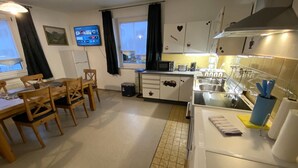 A compact kitchen with a dining area, a TV mounted on the wall, and a window with curtains.