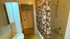 A bathroom with a sink, a bathtub, and a shower. There is a mirror above the sink and a door with a decorative wall.