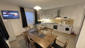 A compact kitchen with a dining area, a TV mounted on the wall, and a window with curtains.