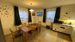 A compact kitchen with a dining area, a clock, a TV, and a microwave.
