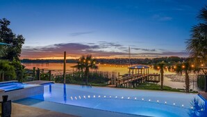 A pool area with a view of a lake at dusk, surrounded by palm trees and a gazebo.
