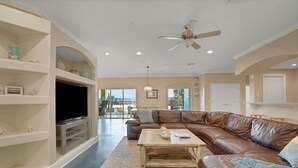 A spacious living room with a brown leather couch, a wooden coffee table, and a television on a stand.