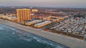 An aerial view of a coastal area with a large hotel, multiple apartment buildings, and a parking lot with RVs.