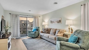 A living room with a sofa, armchairs, a flat-screen TV, and a large window with curtains.
