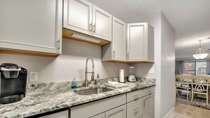 A kitchen with white cabinets, a granite countertop, a coffee maker, and a sink.