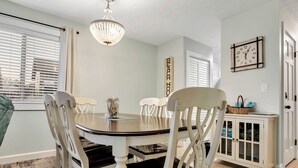 A dining area with a round table, white chairs, a chandelier, and a cabinet with glass doors.