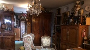 Une pièce meublée de meubles anciens, notamment un buffet en bois, une chaise recouverte d’un tissu à motifs floraux et un lustre.