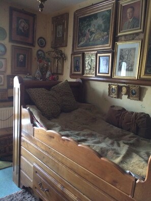 A bedroom with a wooden bed, a dresser, and a wall adorned with framed pictures and a crucifix. - Common Room (Rennes)