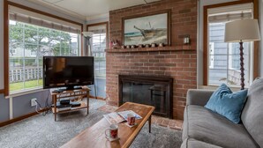 A living room with a TV, fireplace, and a couch. - Perfect Beach Cottage, Friendly, Walk to Beach and Seaside Promenade (Seaside)