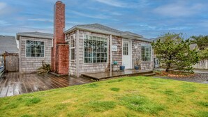 A two-story house with a brick chimney, large windows, and a wooden deck. - Perfect Beach Cottage, Friendly, Walk to Beach and Seaside Promenade (Seaside)