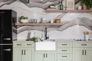 Una cocina con salpicadero de mármol, un refrigerador negro y armarios verde claro.