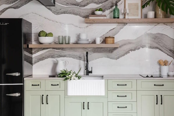 A kitchen with a marble backsplash, a black refrigerator, light green cabinets, and a wooden shelf with various items. - Cozy Modern Studio Just 2 Blocks To Forsyth Park! (Savannah)
