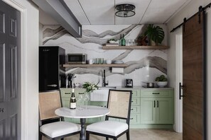 A kitchen with a marble backsplash, a dining table with chairs, and a refrigerator. - Cozy Modern Studio Just 2 Blocks To Forsyth Park! (Savannah)