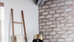 A green sofa with pillows, a wooden ladder, a brass lamp, and a plant on a wooden table. - Cozy Modern Studio Just 2 Blocks To Forsyth Park! (Savannah)