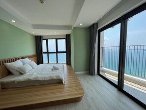 Una habitación de hotel moderna con una cama grande, vistas al mar y un balcón con barandilla.