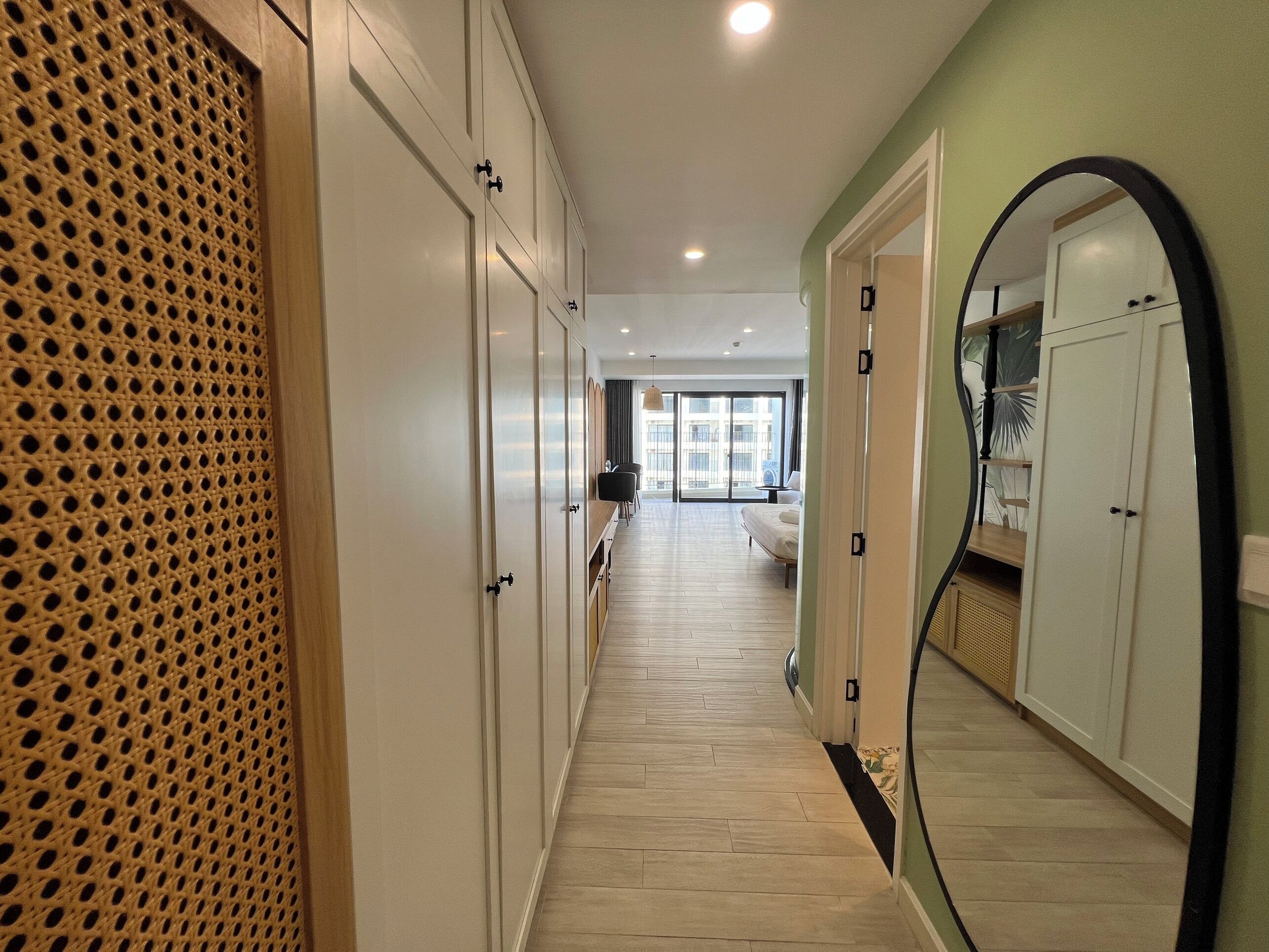 A hallway with a wooden floor, white cabinets, and a large mirror on the right.