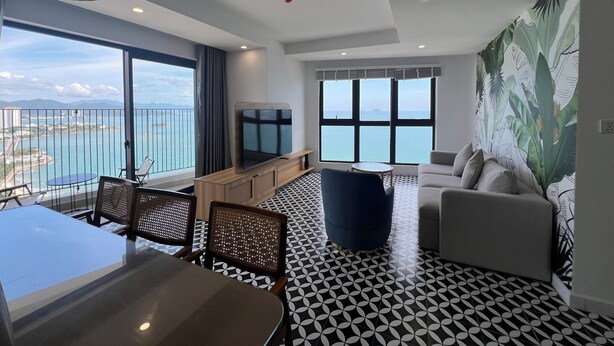 A modern living room with a large window offering a view of the sea, a dining area with a patterned floor, and a seating area with a sofa and armchairs.