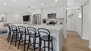 A modern kitchen with white cabinets, stainless steel appliances, and a central island with bar stools. - Charming Coastal 2BR Villa, GOLF CART, Cozy Sunroom, Near Beach, Pool, Wharf. (Miramar Beach)