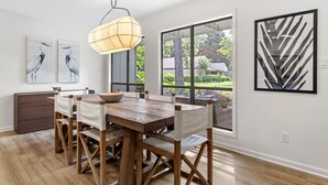 A dining area with a wooden table and chairs, a hanging light fixture, and artwork on the walls. - Charming Coastal 2BR Villa, GOLF CART, Cozy Sunroom, Near Beach, Pool, Wharf. (Miramar Beach)