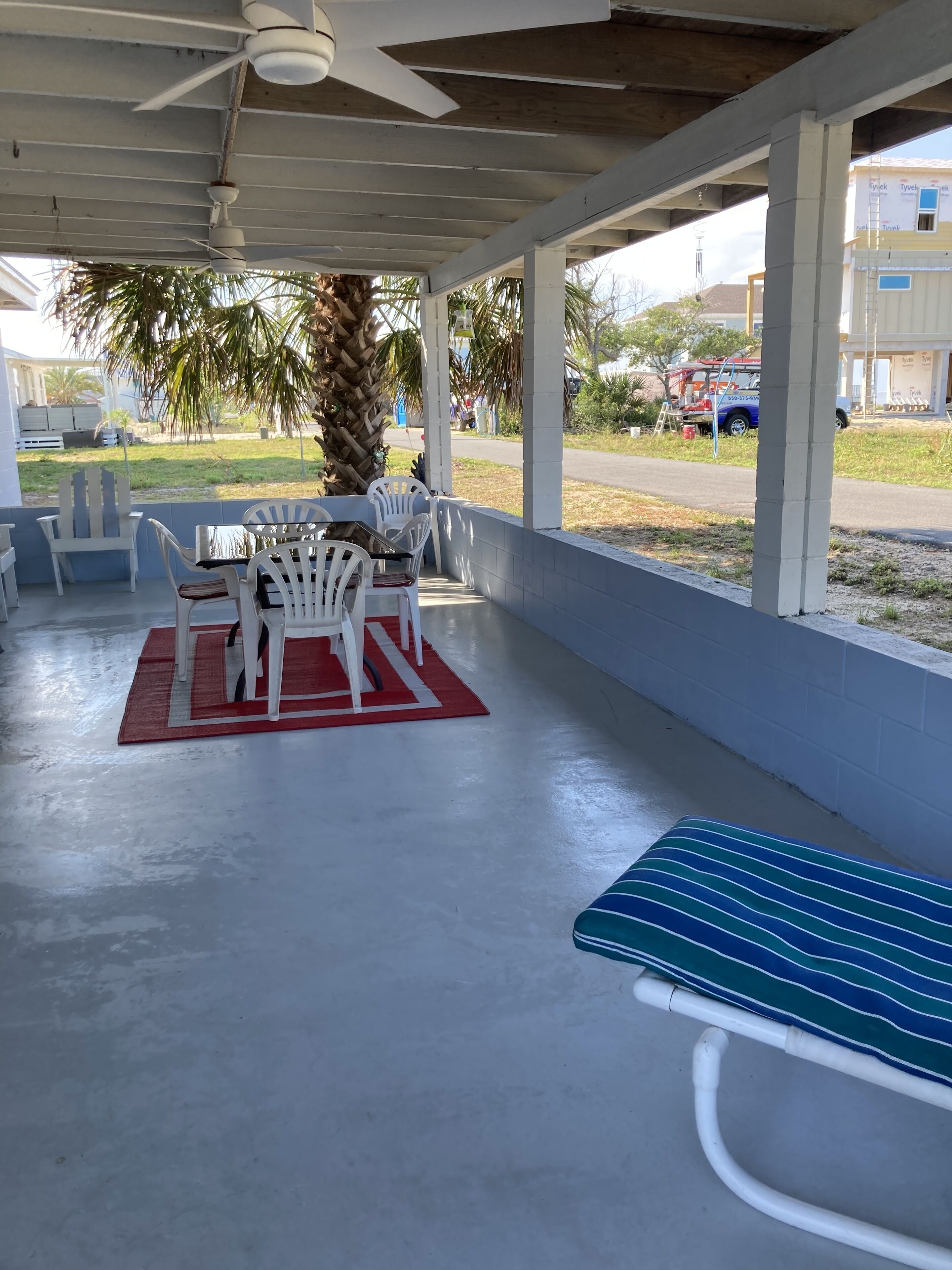 Een overdekt terras met een tafel, stoelen en een enkele lounge stoel, met een palmboom.