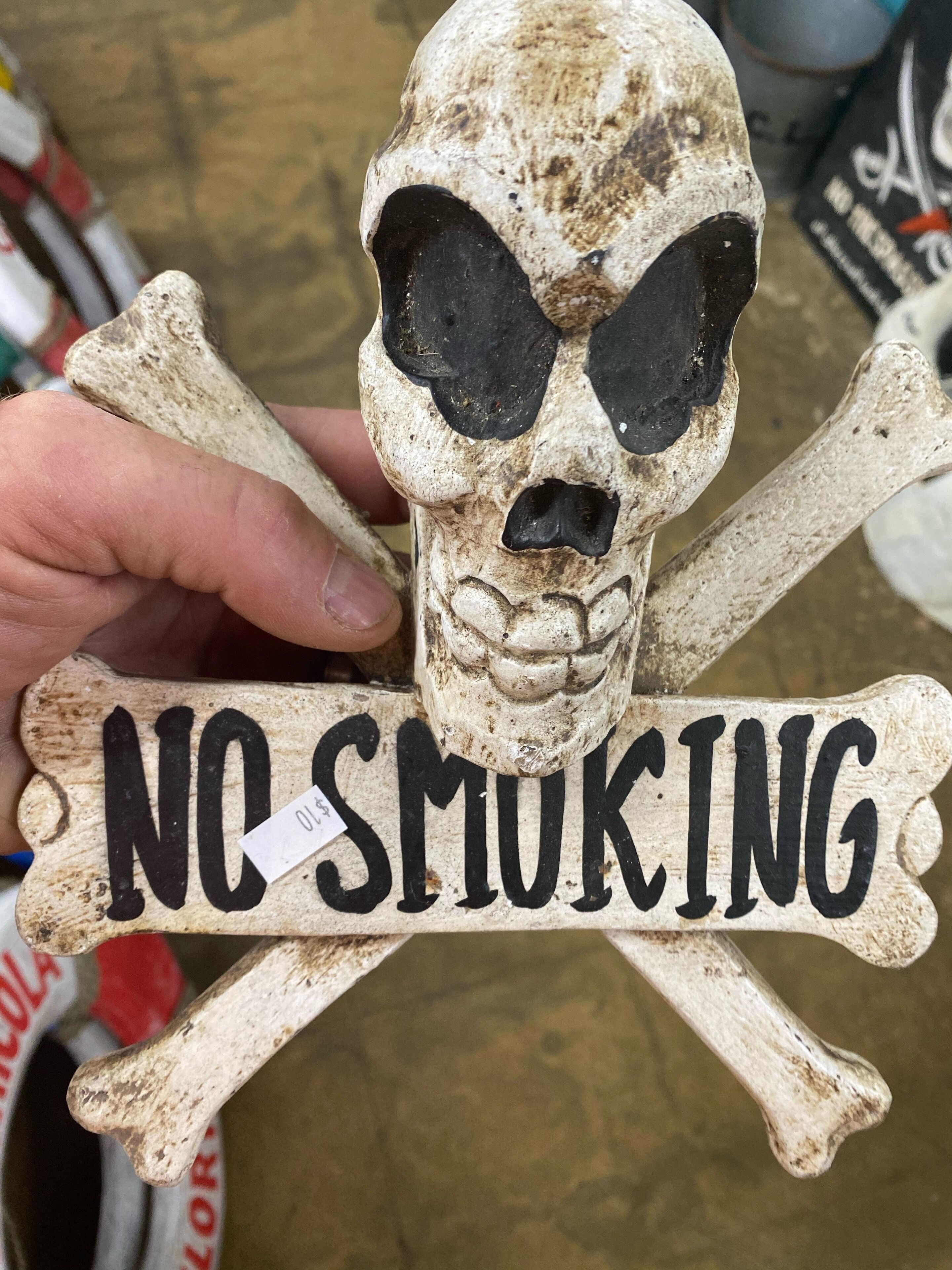 Eine Hand hält ein schild in Form eines Schädels mit der Aufschrift 'NO SMOKING'.