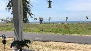 Uma área externa coberta com vista para o oceano, uma cadeira branca e um candeeiro pendente.