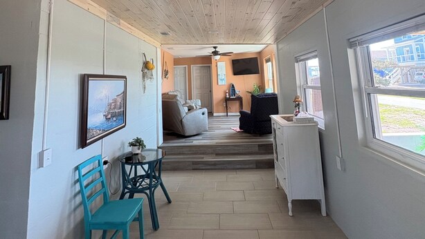 Um quarto espaçoso com teto de madeira, área de refeições com cadeiras, sofá e televisão fixada na parede.