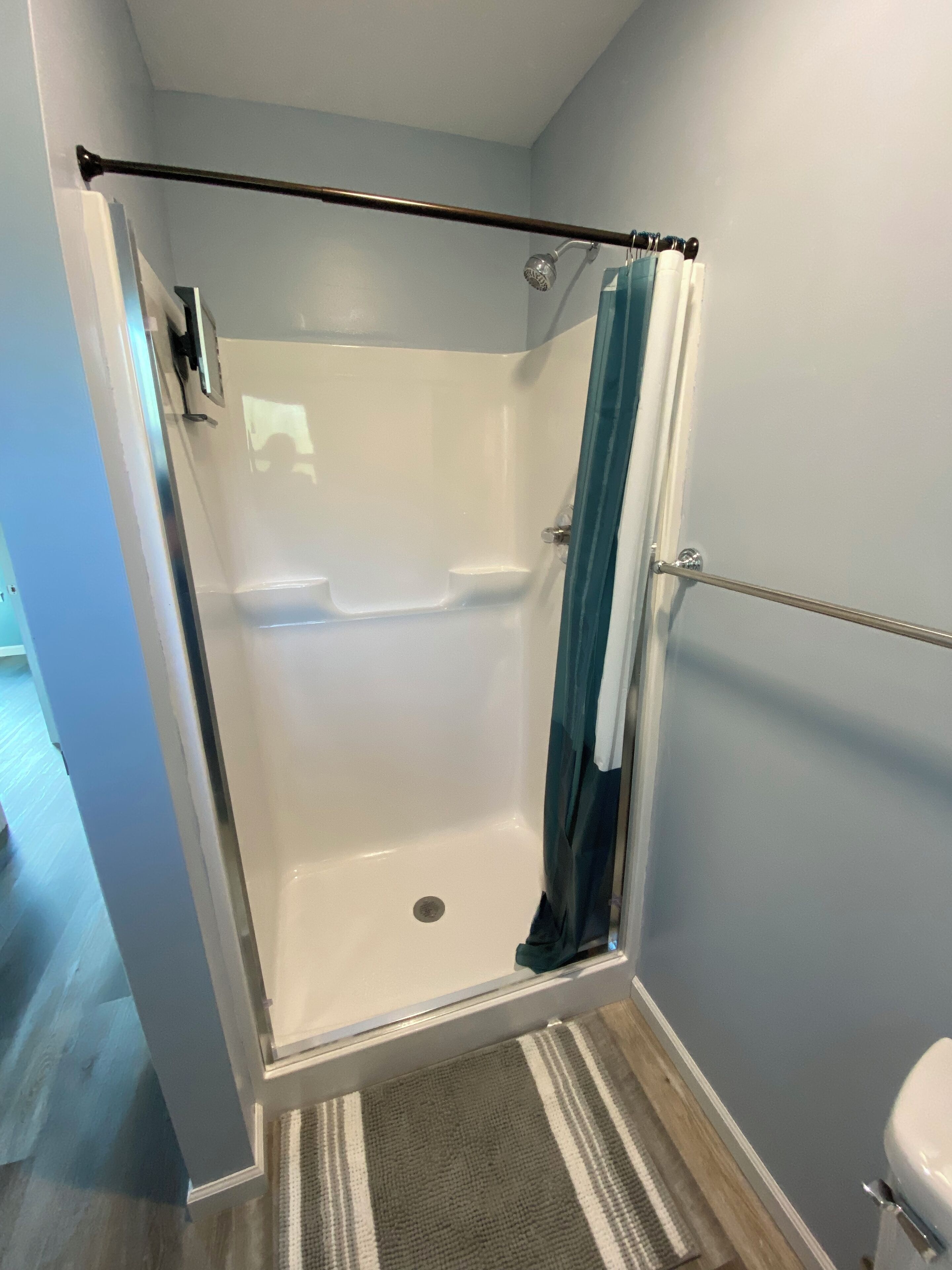 A glass-enclosed shower with a metal frame, a white toilet, and a striped rug on the floor.