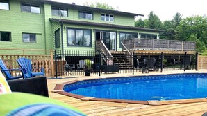 Uma área de piscina com deck de madeira, espreguiçadeiras e um terraço coberto.