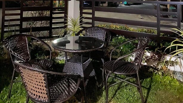 An outdoor seating area with tables and chairs under a large umbrella, surrounded by a wooden fence and greenery.