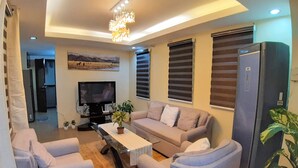 A modern living room with a sofa, two armchairs, a coffee table, a TV, and a refrigerator.