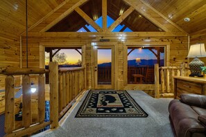 A wooden cabin interior with a cozy fireplace, a welcome sign, and a view of the mountains through the doors. - Ultimate Mountain Retreat: Secluded Cabin + Stunning Views + Hot Tub + Game Room (Sevierville)
