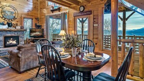 Ein gemütliches Holzhaus-Interieur mit Kamin, Essbereich und Panoramablick auf die Berge.