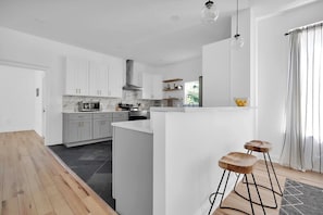 Een moderne keuken met witte kasten, een marmeren spatwand en een centraal eiland met krukken.