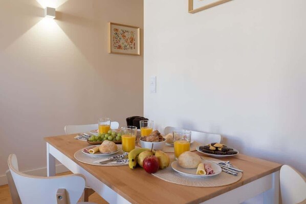 Una mesa de desayuno con platos de comida, vasos de jugo de naranja y un bol de fruta.