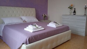 A neatly made bed with a purple bedspread and white pillows, a white dresser with a mirror, and a nightstand with a vase of flowers and a candle. - CasaGiorgio a stone's throw from the historic center (Firenze)