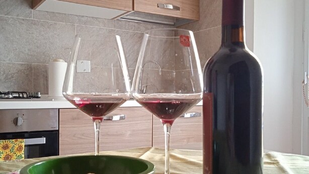 A kitchen with wooden cabinets, a wine bottle, two wine glasses, and a green bowl on a table. - CasaGiorgio a stone's throw from the historic center (Firenze)