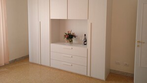 A white wardrobe with multiple drawers and a shelf, a small vase with flowers, and a bottle of wine. - CasaGiorgio a stone's throw from the historic center (Firenze)