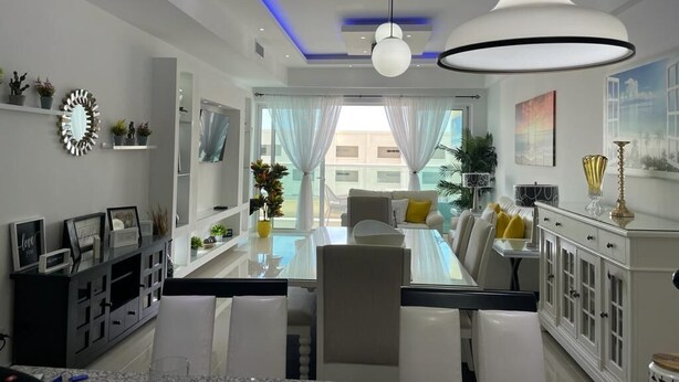 Un comedor moderno con una mesa de vidrio, sillas blancas y un armario blanco con puertas de cristal.