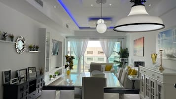 Un comedor moderno con una mesa de vidrio, sillas blancas y un armario blanco con puertas de cristal.