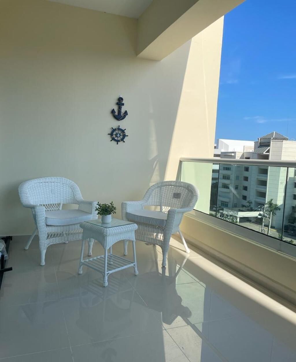 Ein Balkon mit zwei weißen Korbstühlen, einem kleinen Tisch, einem Blumentopf und einer wandmontierten Anker-Dekoration.