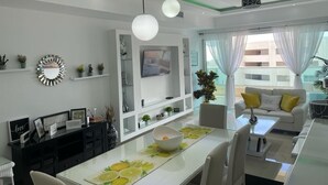 Una sala de estar moderna con un sofá blanco, una mesa de comedor con un cuenco y un televisor en la pared.