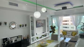 Una sala de estar moderna con un sofá blanco, una mesa de comedor con un cuenco y un televisor en la pared.