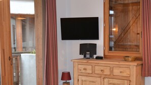 Una habitación con un armario de madera, un televisor de pantalla plana, una mesita con una lámpara y una puerta corrediza de vidrio que da a un área exterior.