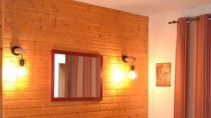 Una habitación con pared de madera, un sofá azul, un espejo y dos luces fijadas en la pared.