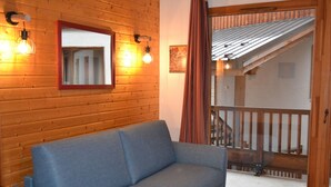 Una habitación con un sofá azul, paredes de madera, una escalera de madera y un balcón con barandilla.
