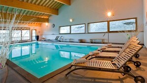 Una piscina interior con sillones de descanso, vigas de madera y cuadros con paisajes nevados.