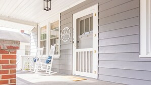 Eine Veranda mit weißen Schaukelstühlen und einer Tür mit rundem Fenster.