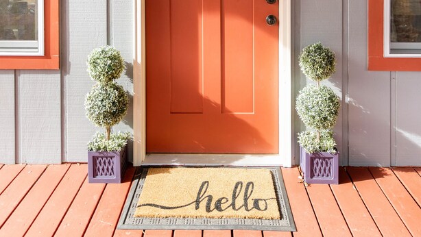 A wooden door with a red frame, a doormat with "hello" written on it, and two small potted plants on either side.